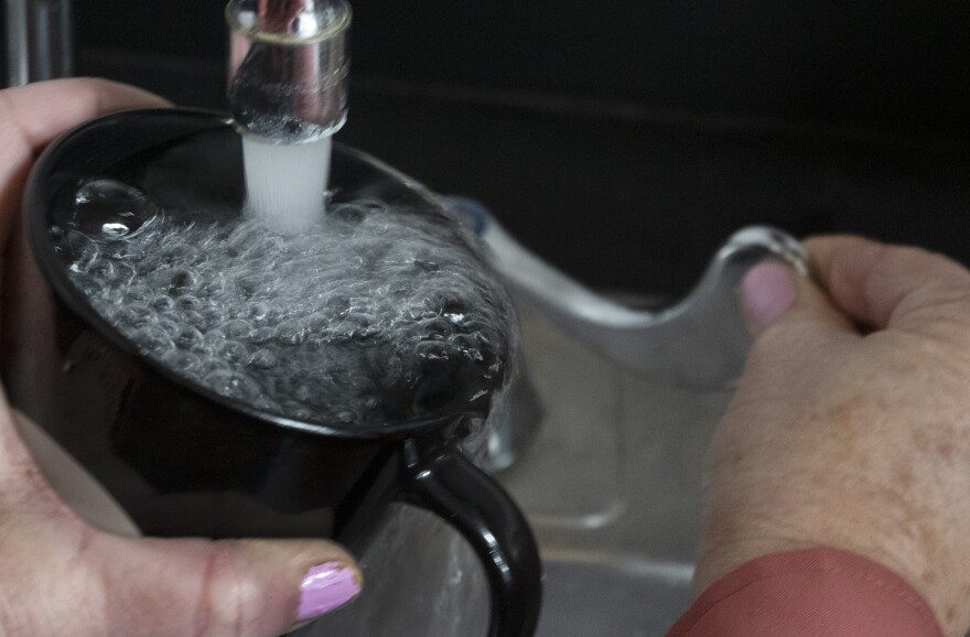 A woman's hand holds a black coffee cup beneath a faucet. Her other hand is turning the lever to run the water.