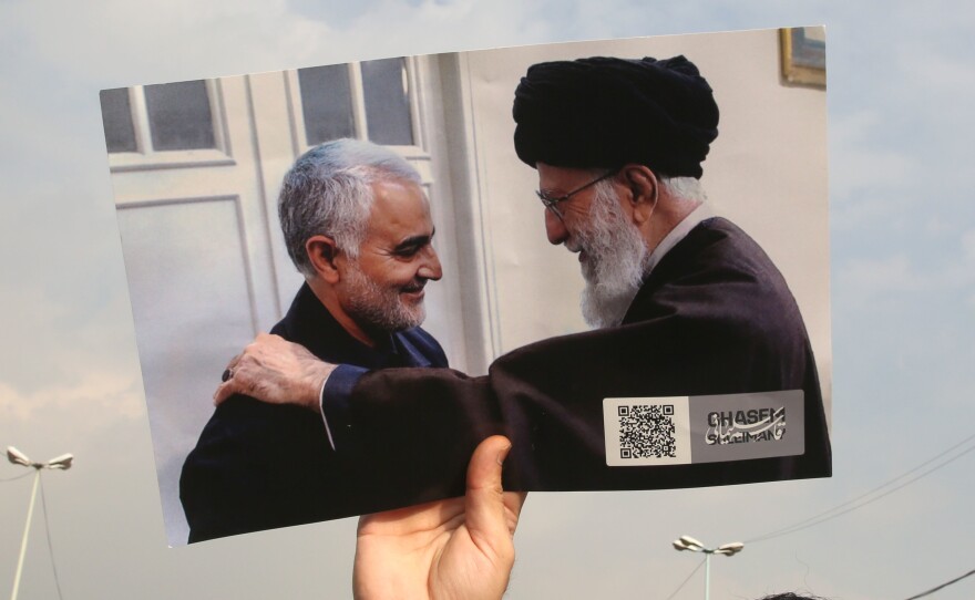 A protester on Friday raises an undated image of Iranian Supreme Leader Ayatollah Ali Khamenei (right) meeting with Iranian Maj. Gen. Qassem Soleimani.