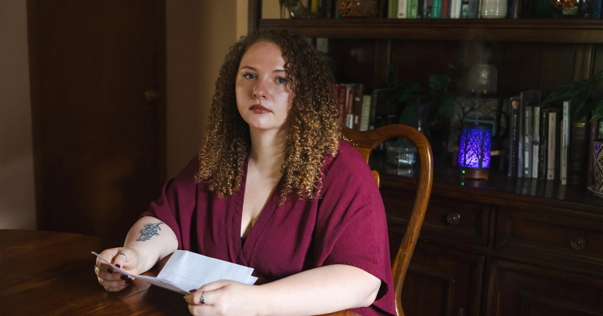 Photo: wusf.org cherubic woman in maroon top with long curly hair sits at a desk holding sheets of paper