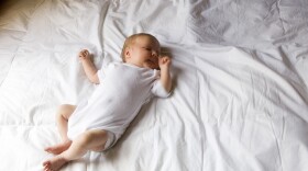 Newborn baby is shown sleeping on a bed.