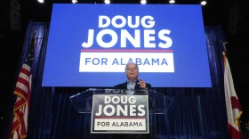 Gubernatorial candidate former Sen. Doug Jones stands behind a podium in front of a screen reading "Doug Jones for Alabama" during an event Friday, Dec. 12, 2025, in Birmingham, Alabama.