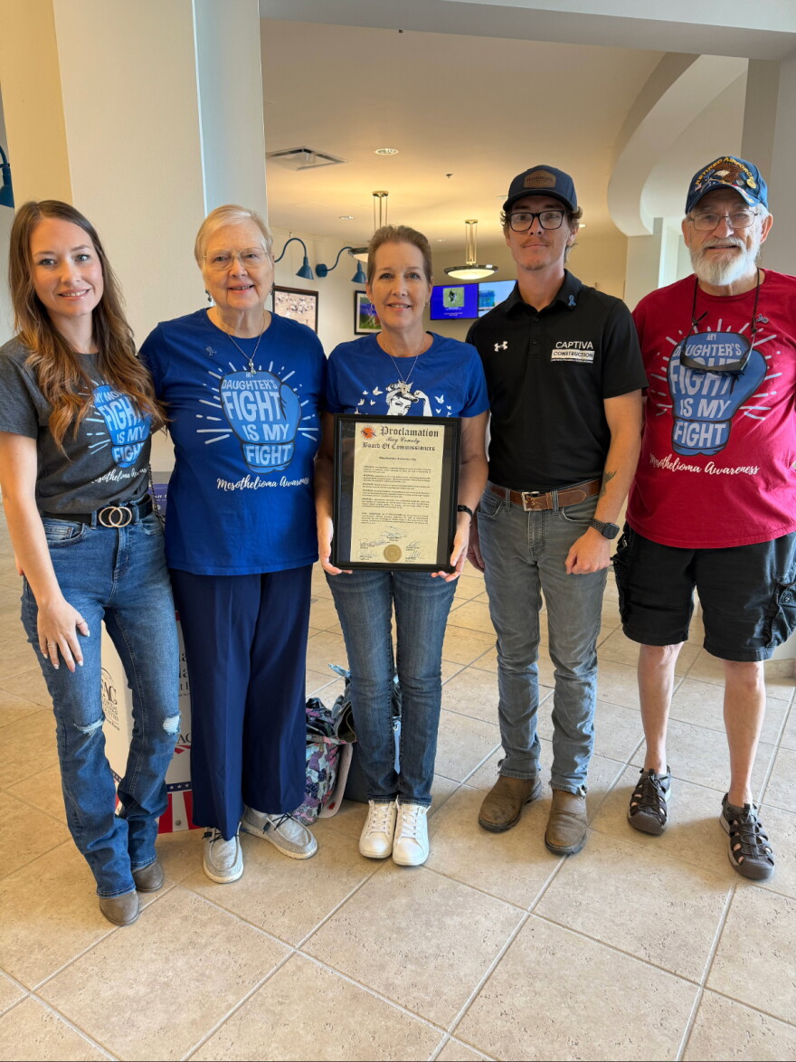 Five people stand side by side wearing shirts that say my daughters fight is my fight. In the middle is a signed proclamation by the bay county commissioners office.