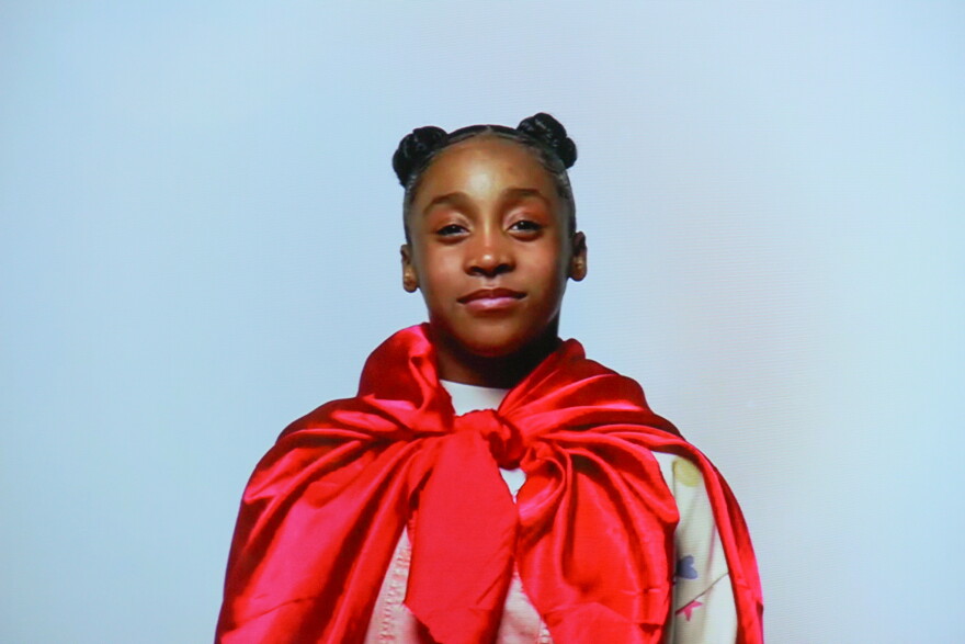 A realistic hologram of a lifesize girl wearing a cape. 