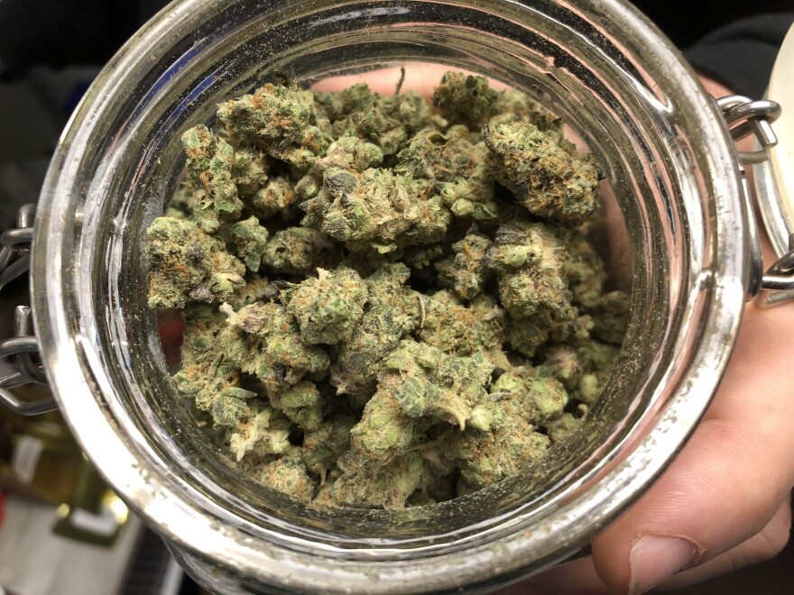 A close-up view looking down into a jar filled with fuzzy green marijuana buds.