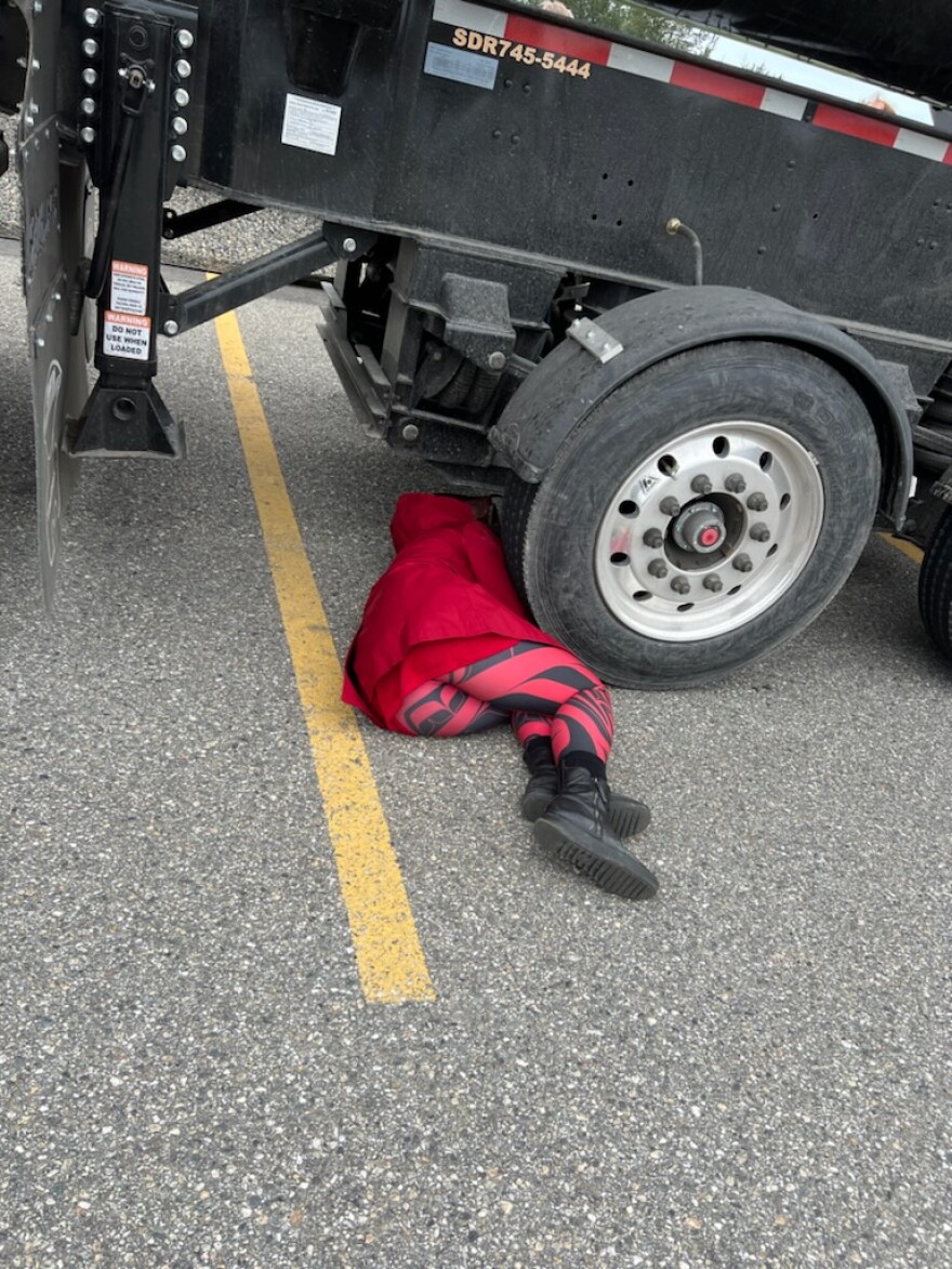 Protester Maya Salganek lies down next to the wheels of the large ore-hauling truck that was just delivered to Black Gold Express for transporting rock from Manh Choh mine near Tetlin to the mill at Ft. Knox.