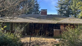 A single story home has a gray roof that is covered in moss. 