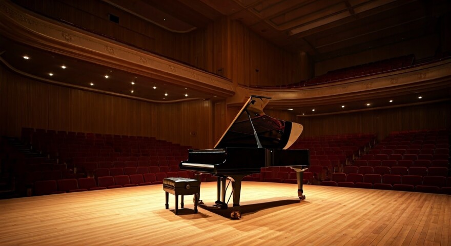 A black grand piano sits on an empty stage.