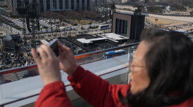 A woman films with her smartphone near a stage for a concert by K-pop group BTS at Gwanghwamun Square in Seoul, South Korea, Friday, March 20, 2026.