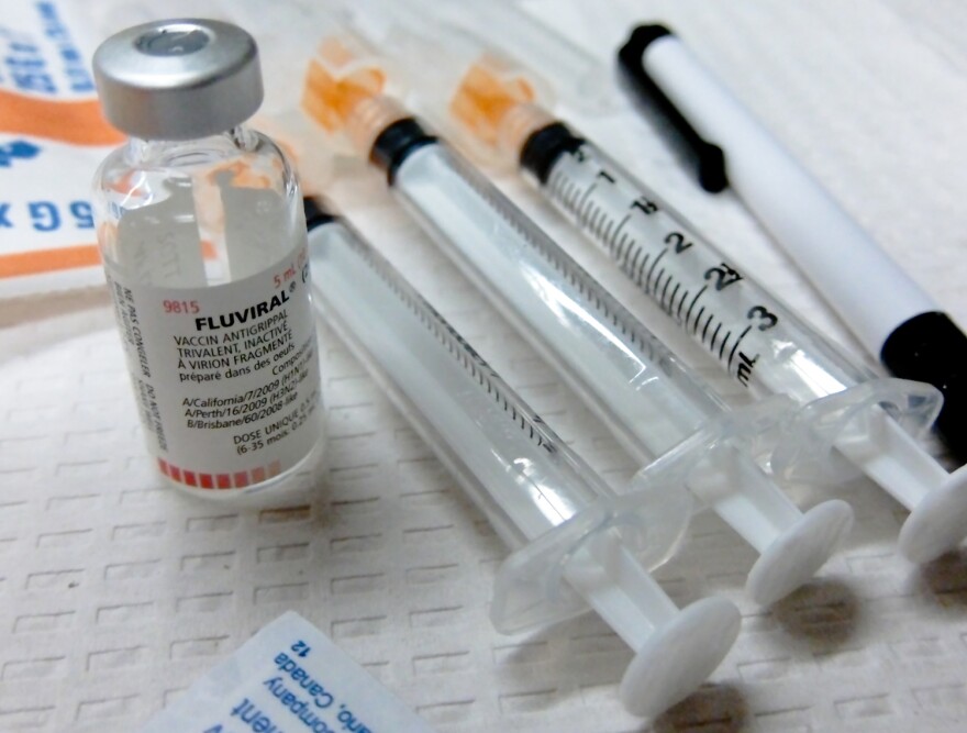 A flu vaccine dose beside several needles.