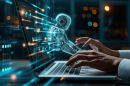 An image of a human with hands above a laptop computer keyboard and a ghostly image of a robot emerging from the screen of the laptop