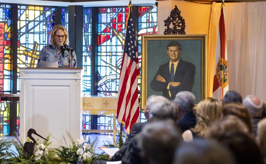 A woman wearing glasses speaks into a microphone at a church lectern.