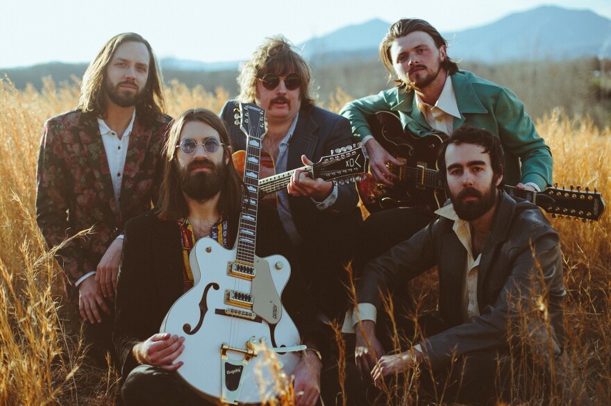 Image of band with guitar sitting in meadow of high grass