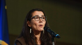 A woman in a black suit jacket speaking into a microphone.