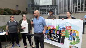 People stand at a press conference in front of a Tacoma court house. They have a banner that reads "Safe Homes For All" 
