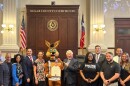 The Spurs Coyote holds a proclamation presented to the team staff, Precinct 1 Commissioner Rebeca Clay-Flores is to the left of the mascot, while County Judge Peter Sakai is to the right. Both are flanked by other elected county leaders and Spurs representatives on Aug. 4, 2026