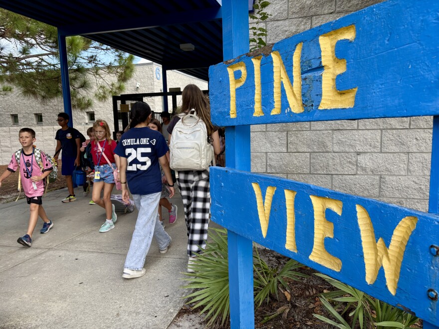 Close-up of a wooden blue and yellow sign that says Pine View with children walking to the left