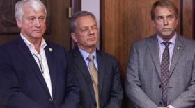 Department of Transportation and Public Facilities Commissioner John MacKinnon, Gov. Mike Dunleavy’s Chief of Staff Ben Stevens, and Senior Policy Advisor Brett Huber watch a press conference unveiling Dunleavy’s budget proposal on Wednesday, December 11, 2019, at the Capitol in Juneau, Alaska. (Rashah McChesney/KTOO)