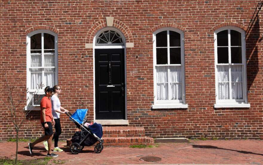 A couple push their child in a stroller along a sidewalk in the Old Town section of Alexandria, Virginia. (Photo by Robert Alexander/Getty Images)