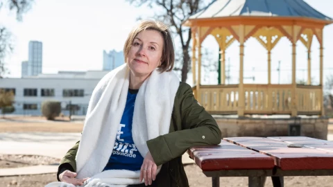 A photo of Julia Roubtsova Hewitt sitting at a picnic table at Crockett Park in San Antonio, she looks at the camera.