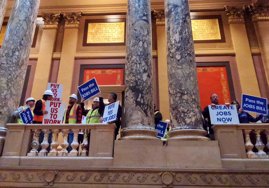 People hold signs saying "Put Us To Work," "Create Jobs Now," Vote Yes For Jobs," and "Pass the Jobs Bill" outside the Minnesota Senate chamber.