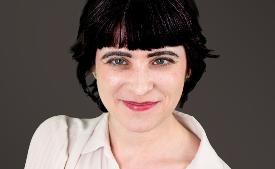 A smiling woman with short dark hair wearing a white button-down shirt.