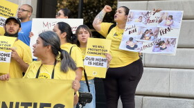 A close up on a crowd protesting with some signs that read, "Our home is here."