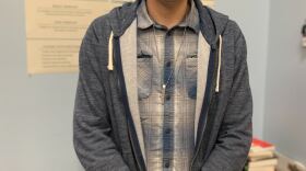 Jayden Perez is standing in the KUNR newsroom. He is looking toward the camera and smiling.