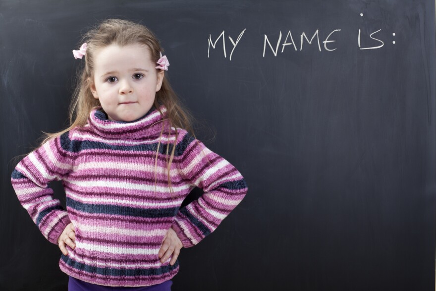 A cute girl in front of a black chalkboard. "My Name is" is written on the board.