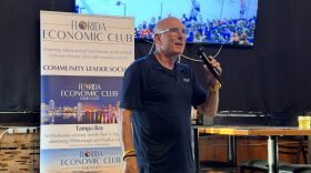 Bald man in glasses with a polo speaks into a microphone 
