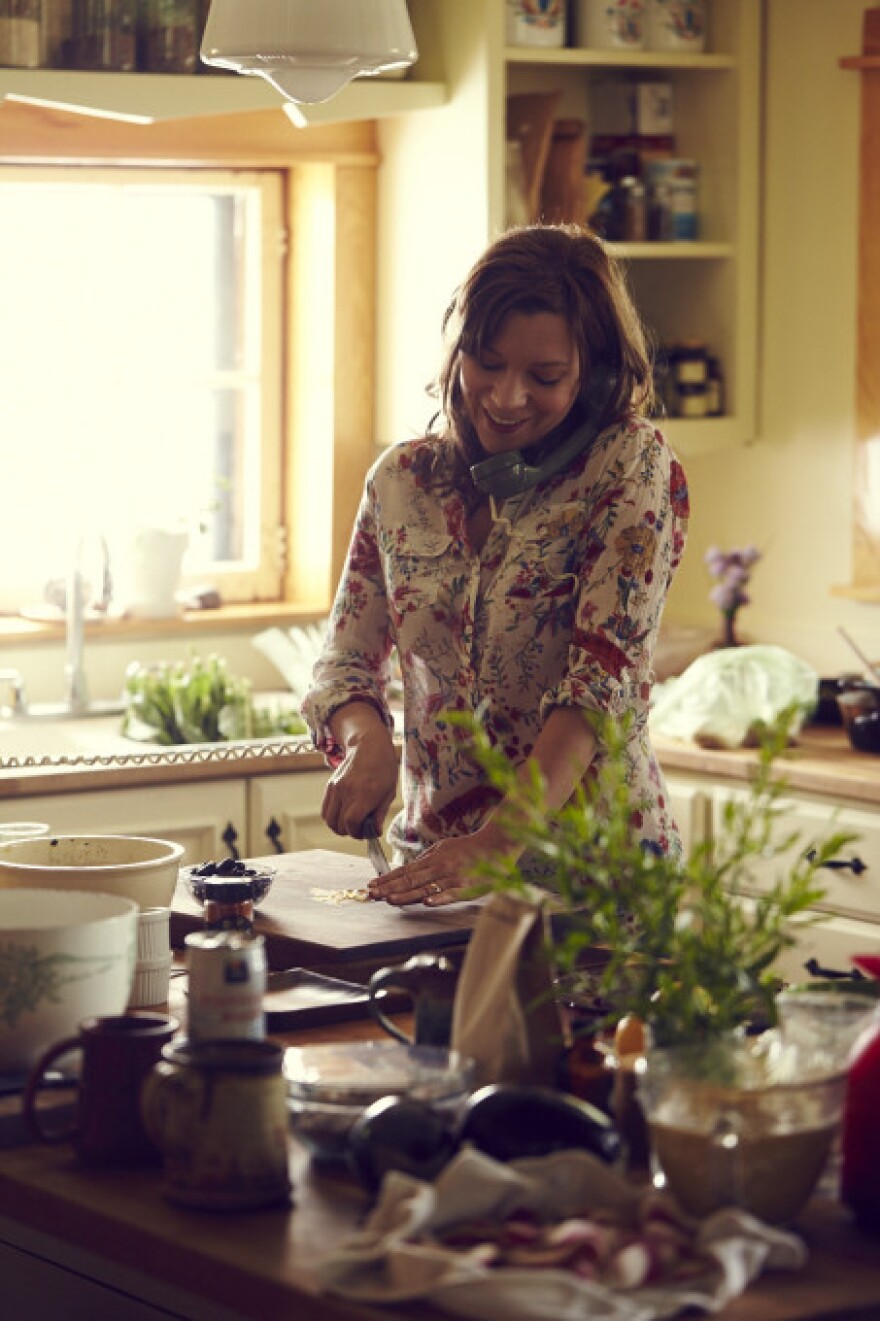 A woman is on the phone in her kitchen preparing food for guests.