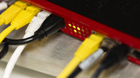 Close-up view of cables plugged into a router, which is red and black with small round green numbered lights.