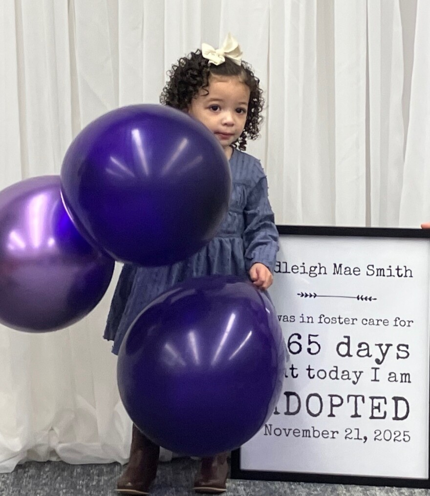 Adleigh Mae, 2 1/2, with a sign noting she was in foster care 865 days before being adopted Nov. 21, 2025.
