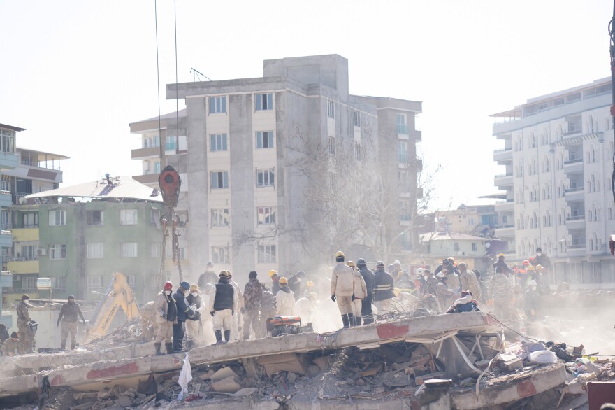 Workers stand in the debris and dust of an apartment building where members of the Demir family lived, as they dig through it looking for people who were in the building when it collapsed.