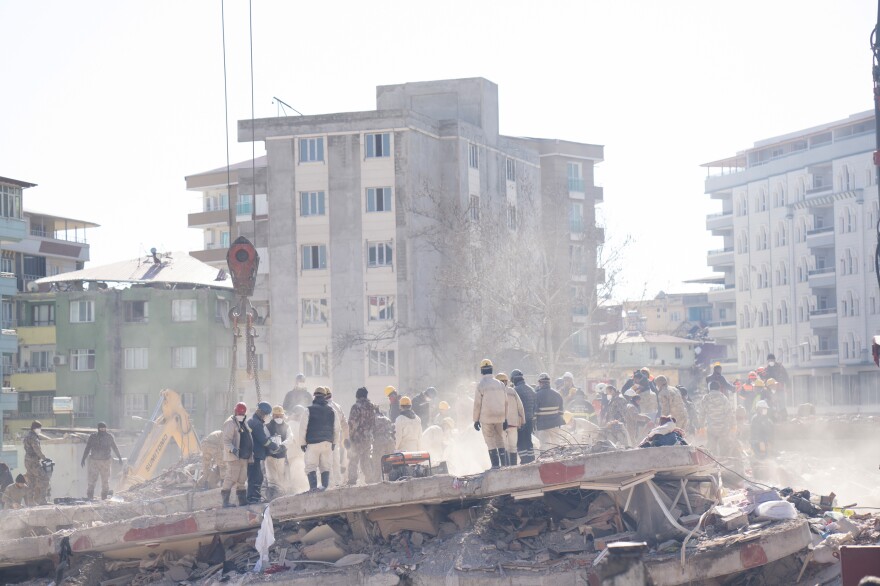 Workers stand in the debris and dust of an apartment building where members of the Demir family lived, as they dig through it looking for people who were in the building when it collapsed.