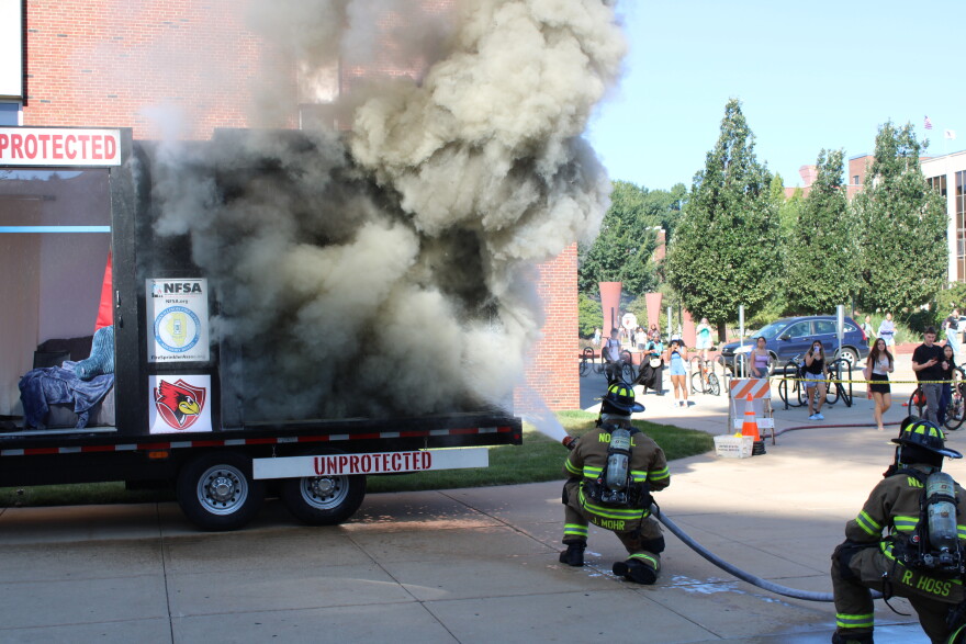 Two firefighters put out a fire in the "unprotected" section of the fire demonstration trailer with a hose.