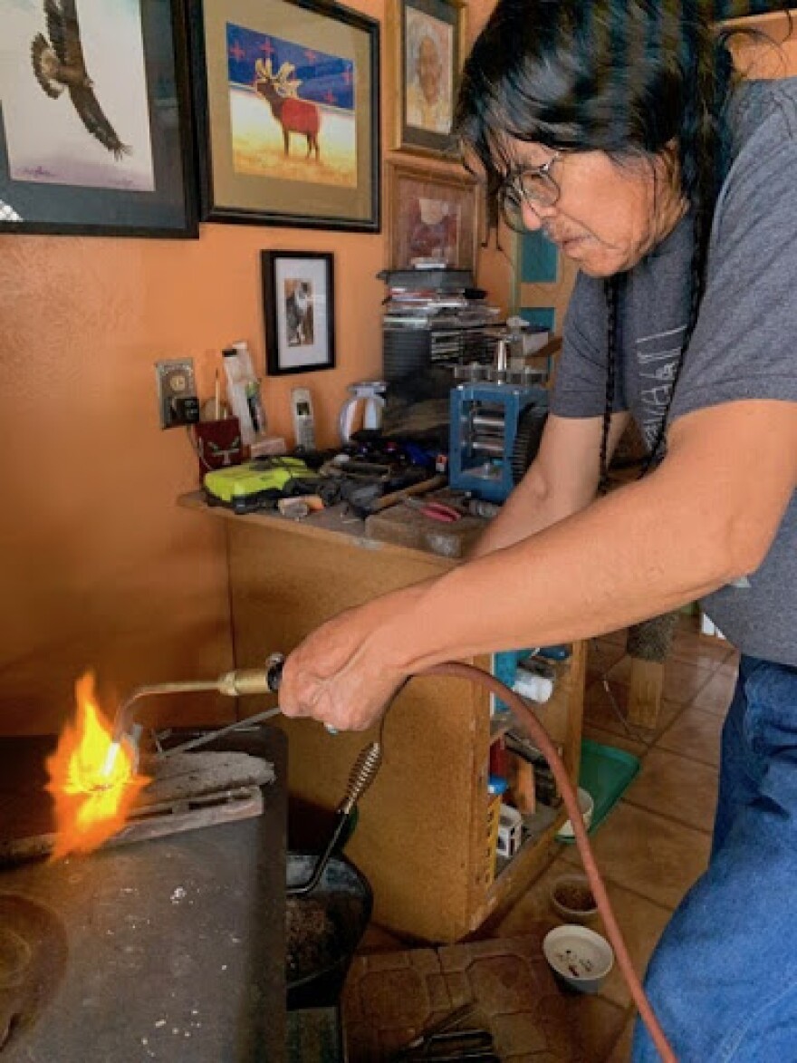 A Navajo man holds a hand torch with flames coming out of the end. 