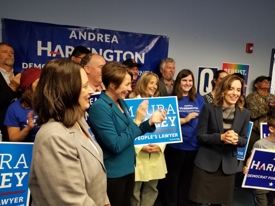 A room full of people stand in front of a large sign that says "Andrea Harrington"