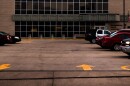 A parking lot sits from a person's view and a building behind it. A few cars are in it. 