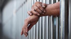 The hands of an unidentified inmate rest outside the bars of a holding cell. 