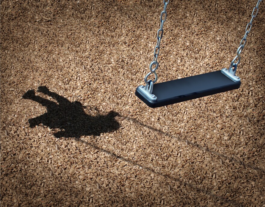 Missing child concept with an empty playground swing and the shadow of a little girl on the park ground.