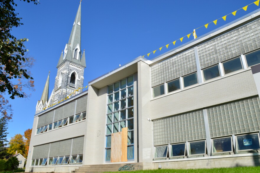 A former school building sits against a blue sky, with green grass.