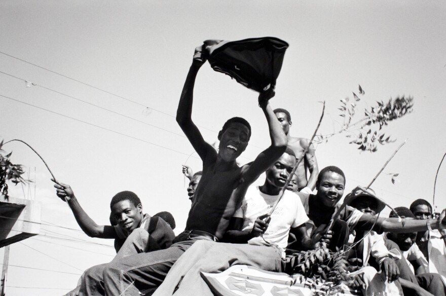 "February 7, Port-au-Prince." Students wave green branches and pieces of uniforms torn from the Tontons Macoute as they enter the capital on a tap-tap, a vehicle. The Tontons Macoute was a paramilitary group that terrorized citizens. It is part of an exhibition opening Friday, Dec. 19 at the Chrysler Museum of Art.