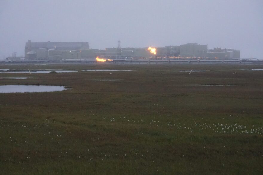 Flames seen above and in front of a large industrial facility on a foggy plain