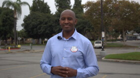 A man with a tennis-ball-sized-pin on his shirt that reads "CALL KEVIN!," stands in a parking lot with his hands together at his torso