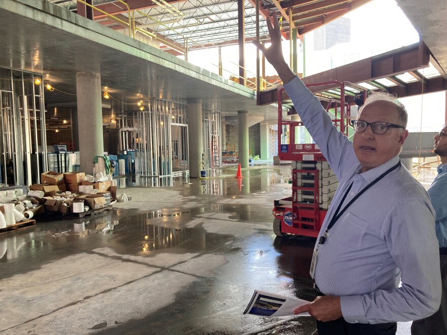 Steve Dubnik, president and CEO of The Strong National Museum of Play, stands in the future entry hall and motions toward the upper level of the expansion. The interior shown is a mess of concrete, steel and other metal framework. He is gesturing toward where an oversized Donkey Kong arcade game and other video game exhibits will be located. 