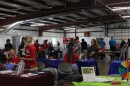 A crowd of people are scattered around a large gathering space with tables and vendors.