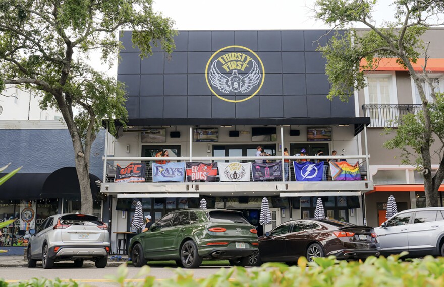 Outside of a sports bar with a balcony and cars parked below 