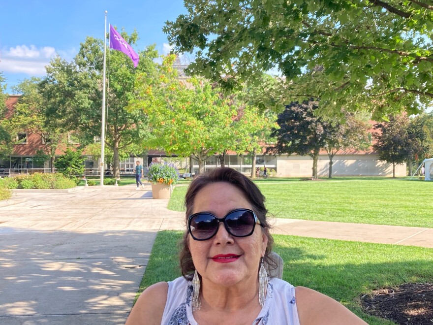 SU spiritual advisor Diane Schenandoah sits on the SU quad near Hendricks Chapel with the Haudenosaunee flag flying behind her.