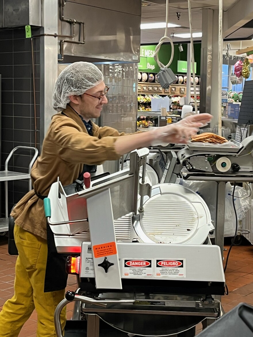 Conor Hall, in a white hairnet and black apron, leans toward a tall scale with food on it in an industrial kitchen.