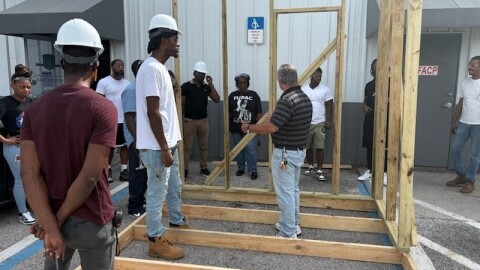 Vocational students with the CDC of Tampa wear hard hats and stand in a parking lot to learn wall framing during an intro-to-construction training for adults.